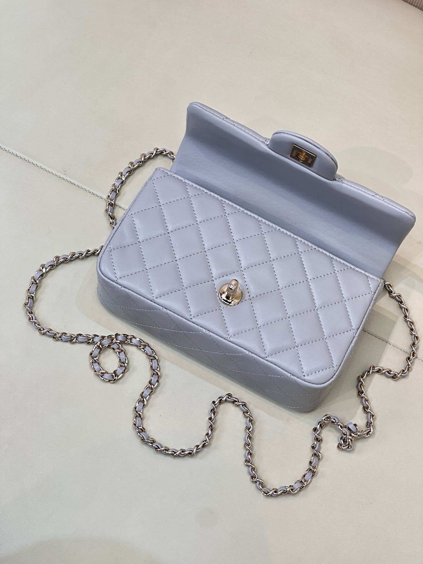 Light blue Chanel flap bag with quilted pattern, gold-tone clasp, and chain shoulder strap.