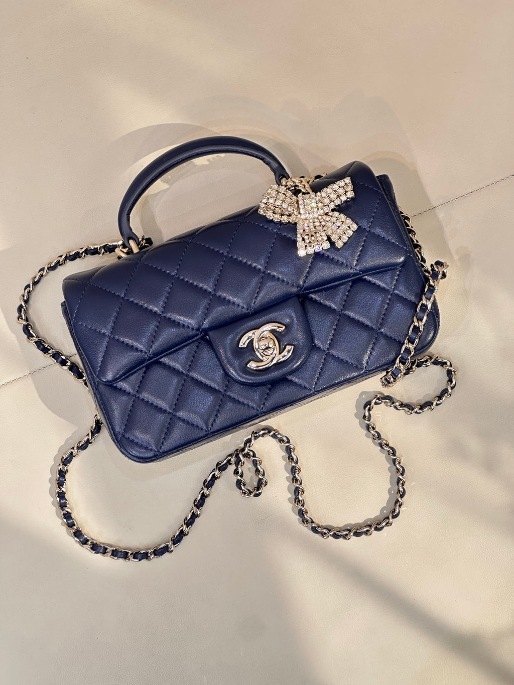 Quilted blue handbag with chain strap, top handle, jeweled bow and front logo emblem
