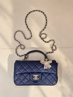 Quilted blue handbag with top handle, chain strap, jeweled bow front and logo plaque