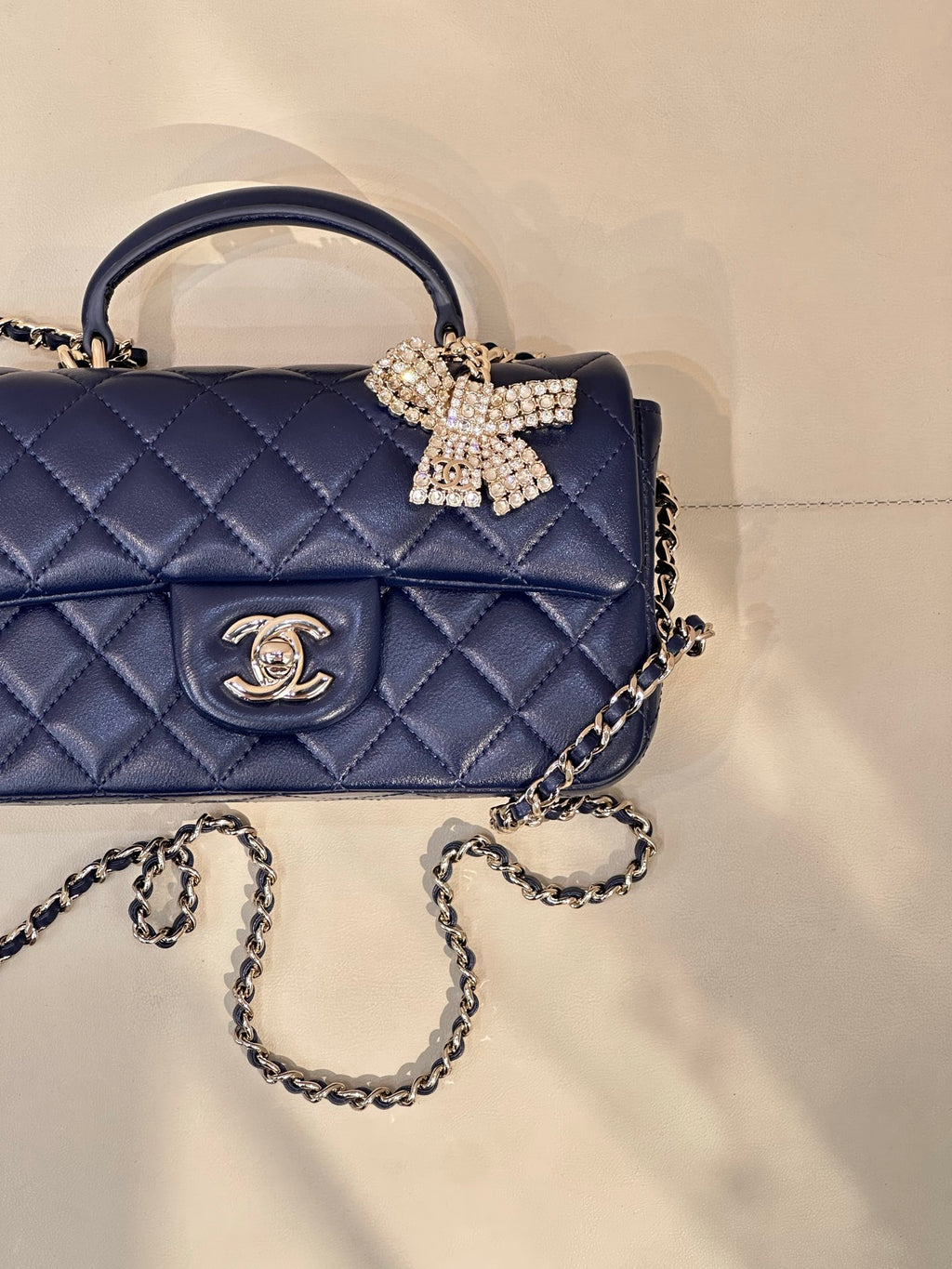 Quilted blue handbag close-up: front logo emblem and jeweled bow with chain strap