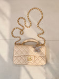 Chanel quilted leather bag with chain strap, top handle, and logo flap in light beige