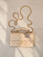 Chanel quilted leather bag with chain strap, top handle, and logo flap in light beige