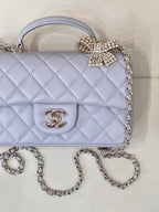 Quilted Chanel flap bag in light blue with gold CC logo and rhinestone bow detail.