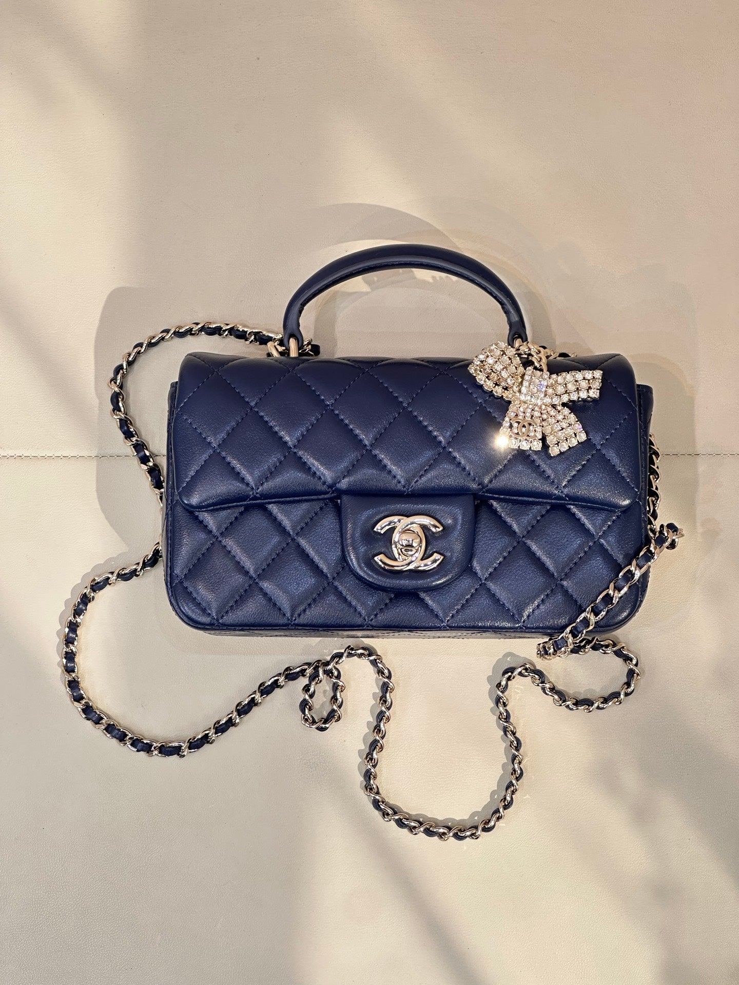 Quilted blue handbag with chain strap, top handle, jeweled bow and logo emblem