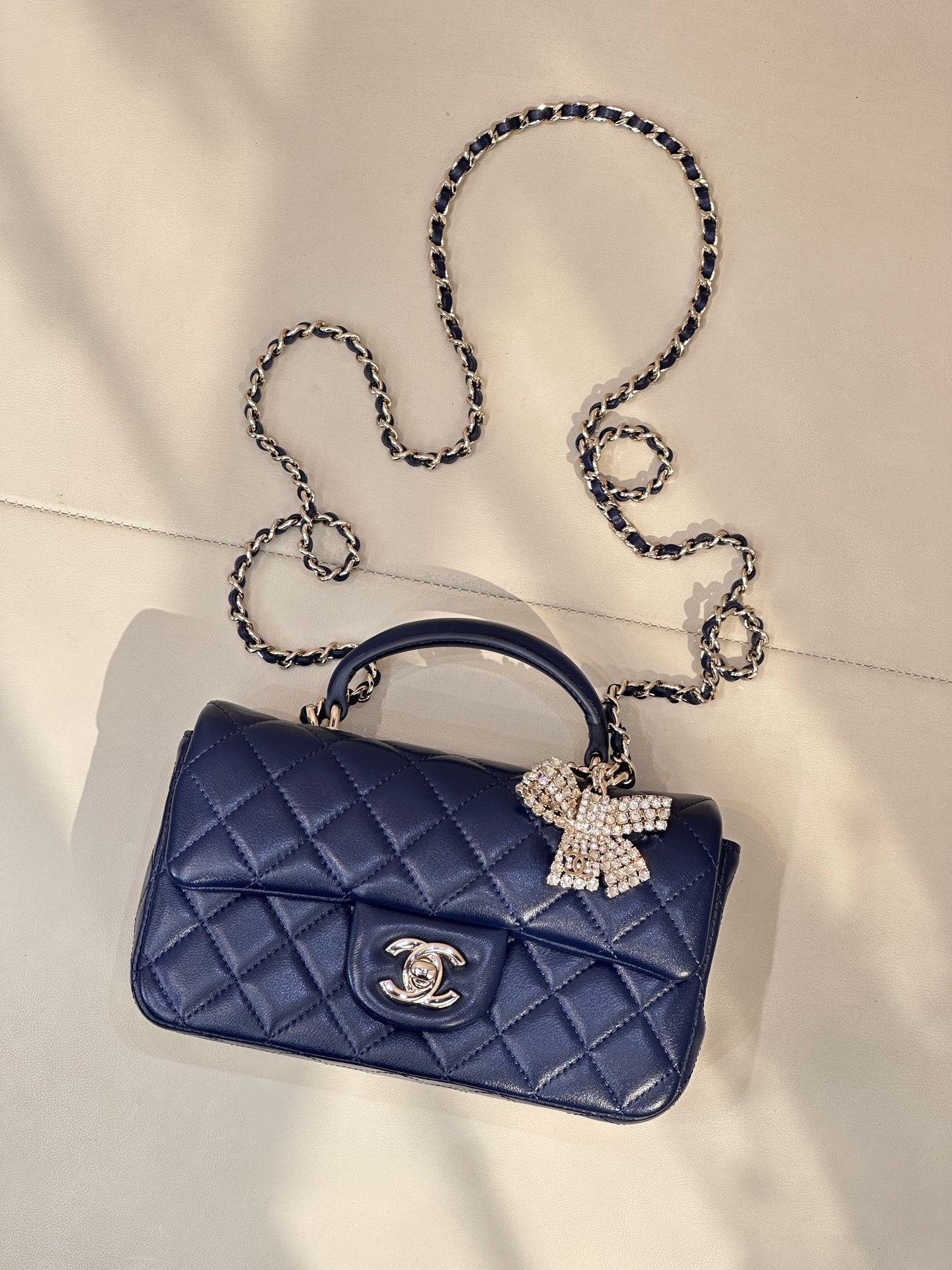 Quilted blue handbag with chain strap, jeweled bow detail and logo plaque
