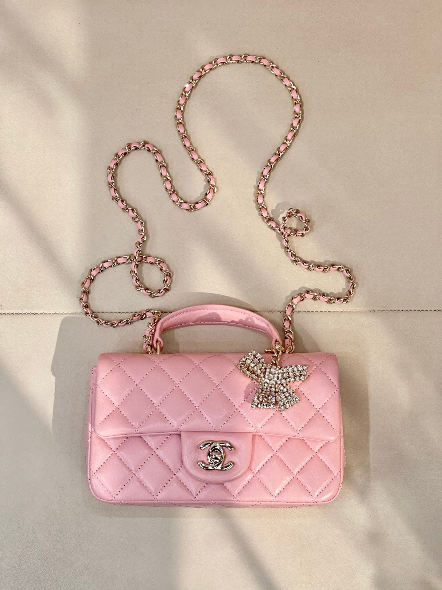 Chanel quilted pink flap bag with rhinestone bow charm, chain strap, and CC logo