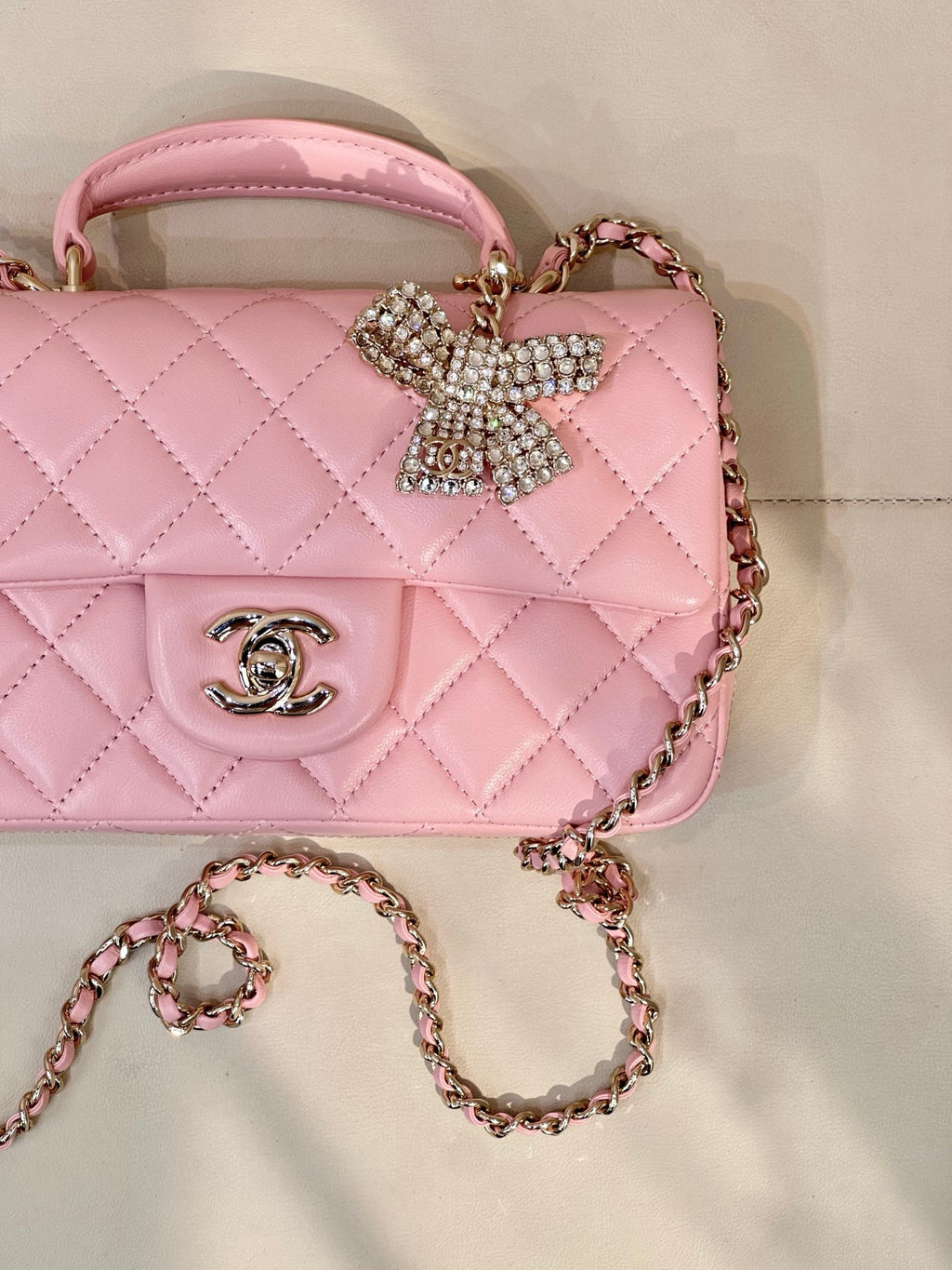 Chanel pink quilted flap bag detail with rhinestone bow, CC emblem, and chain strap