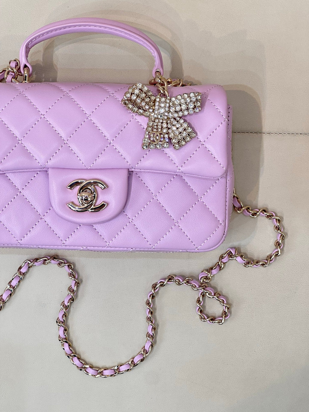 Quilted light purple mini handbag close-up with gold logo emblem and rhinestone bow