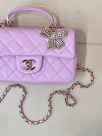 Quilted light purple mini handbag close-up with gold logo emblem and rhinestone bow