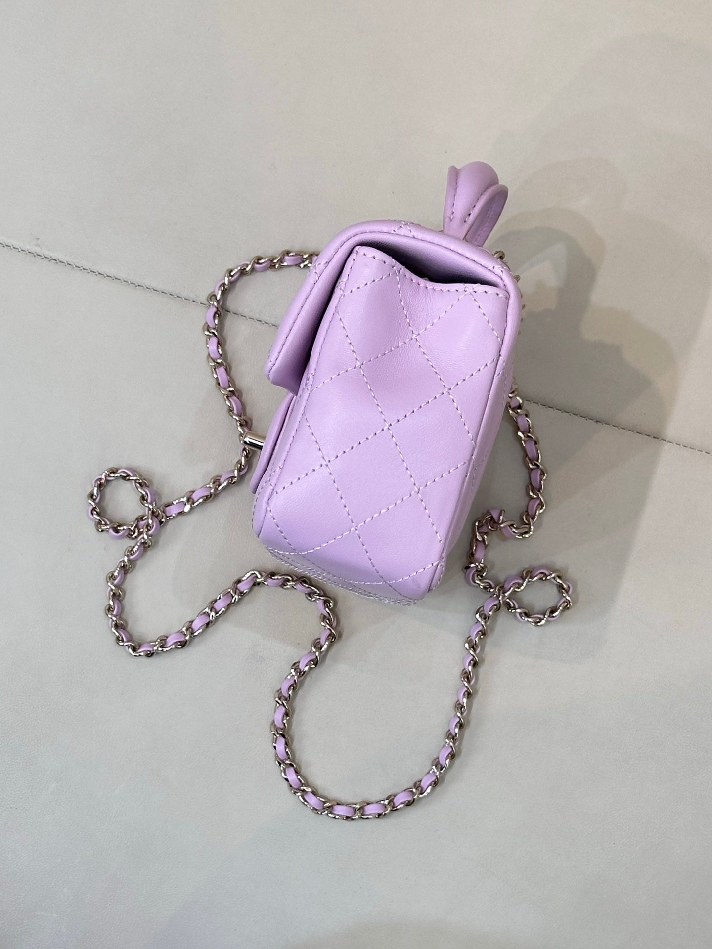 Light purple quilted mini handbag back view with top handle and chain shoulder strap