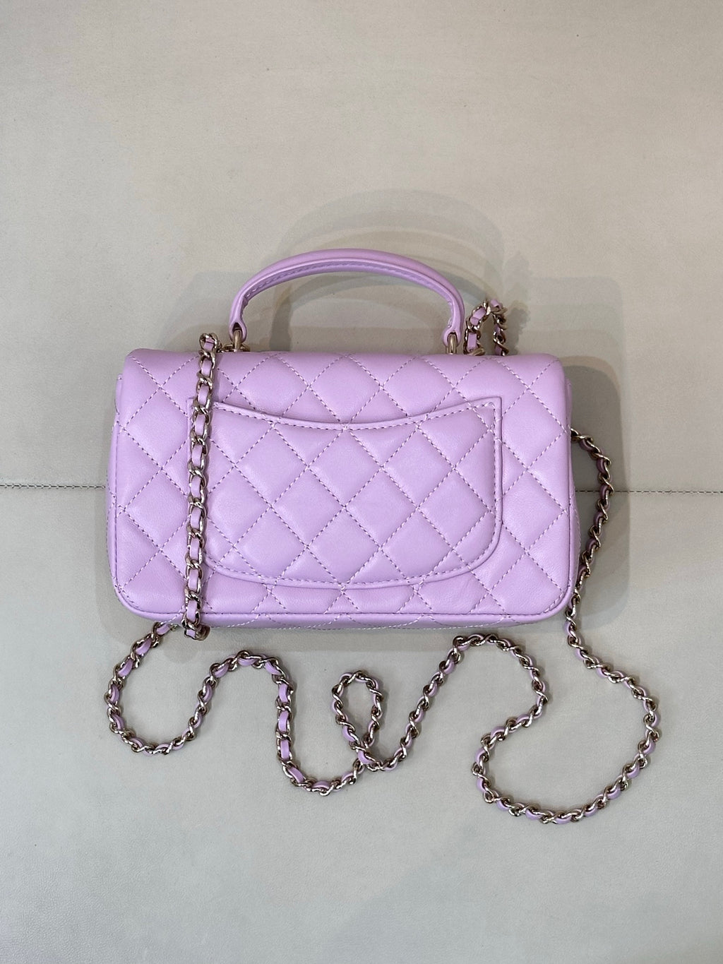Quilted light purple mini handbag with top handle, front flap, and chain crossbody strap