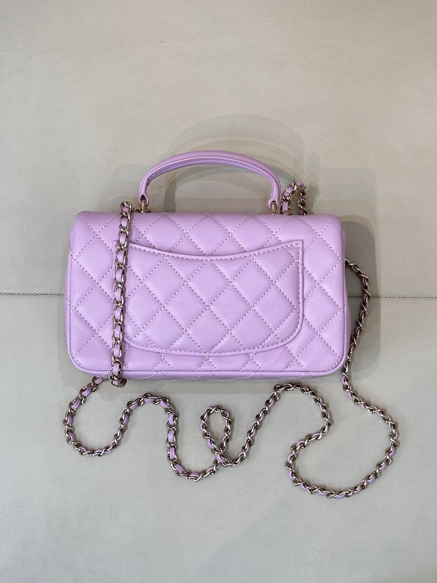 Quilted light purple mini handbag with top handle, front flap, and chain crossbody strap