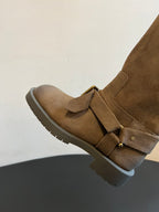 Suede ankle boot with top strap and metal buckle, set on a lug sole.