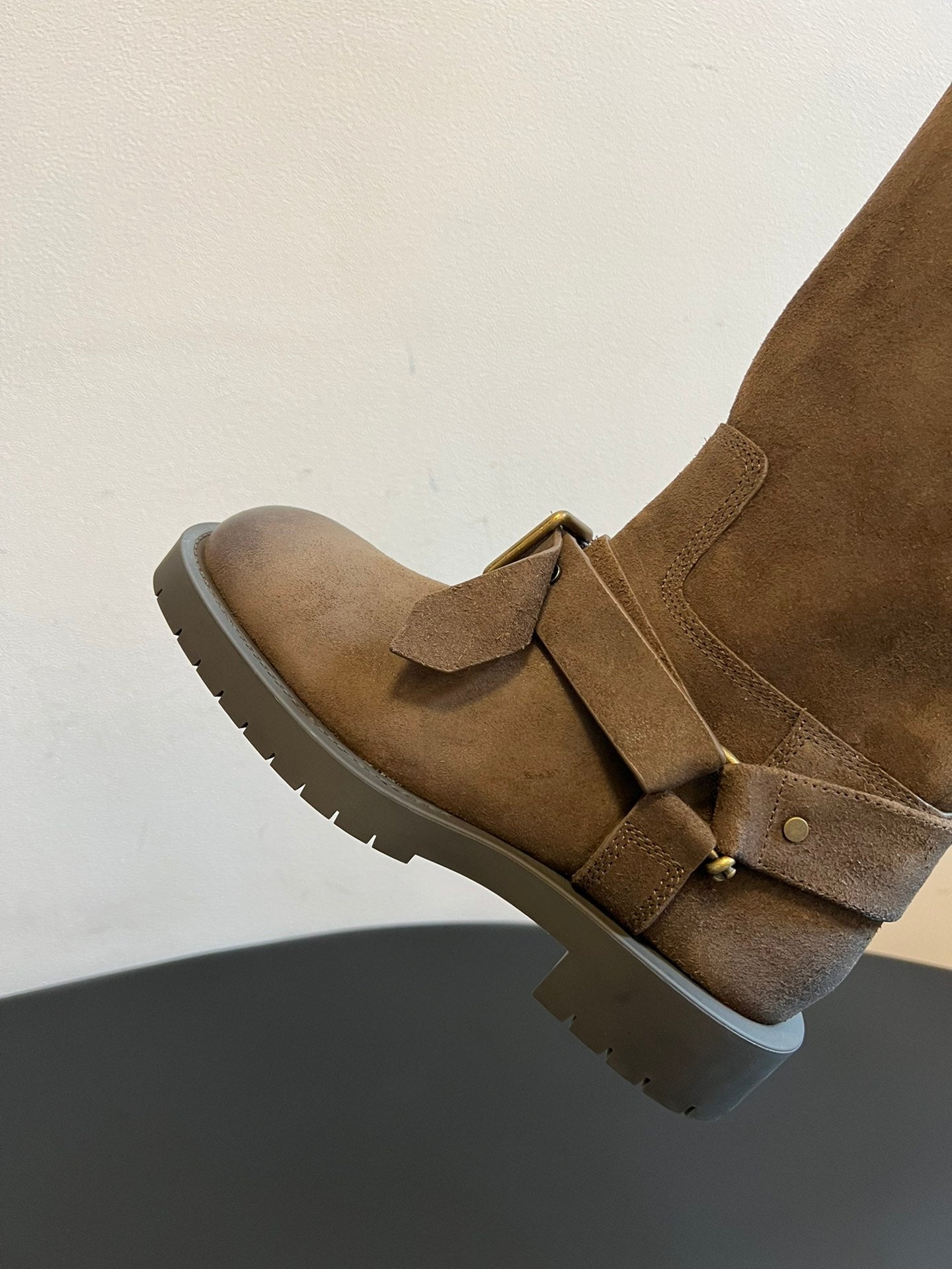 Suede ankle boot with top strap and metal buckle, set on a lug sole.