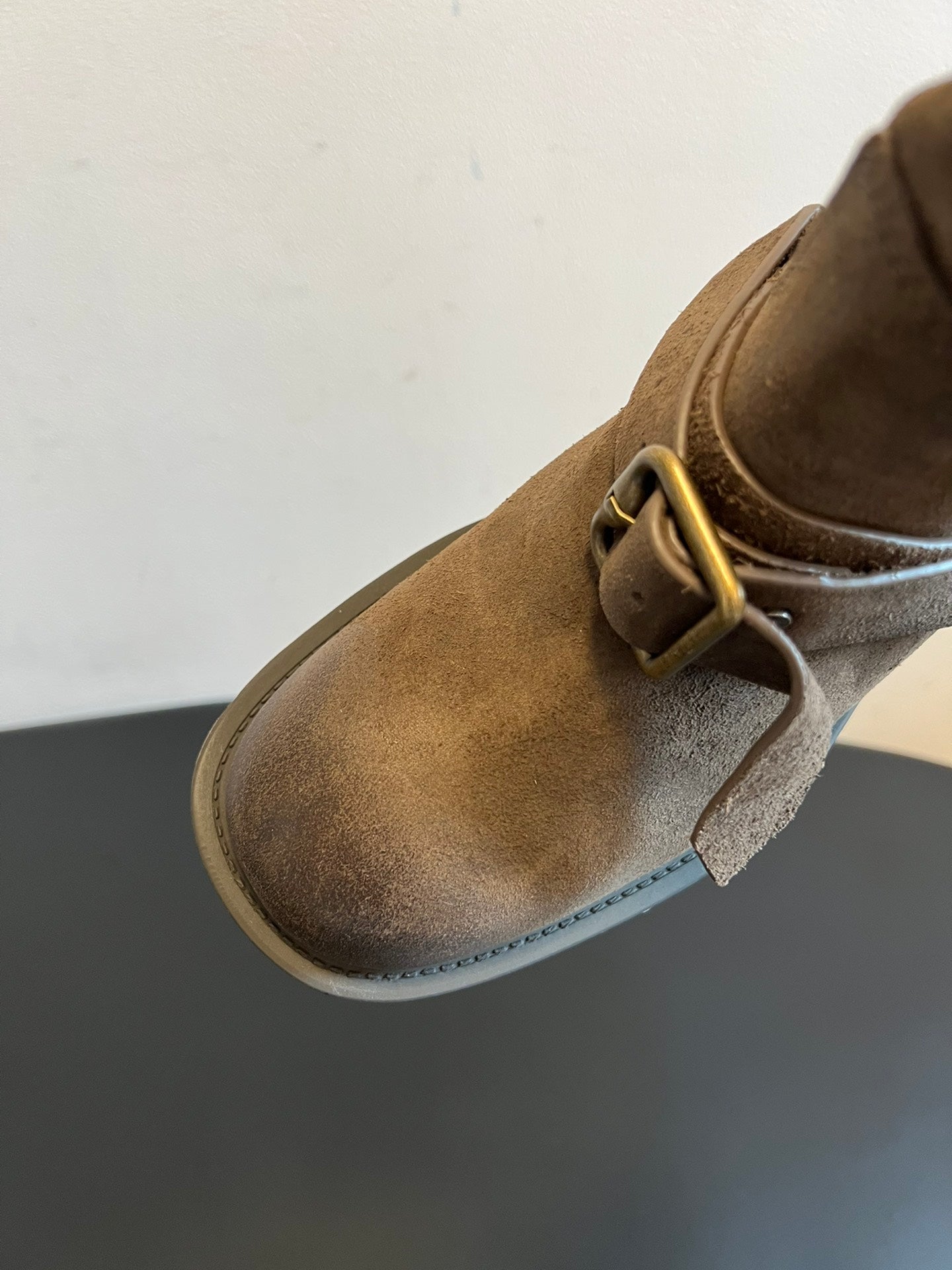 Close-up of suede ankle boot with metal buckle strap and textured upper.