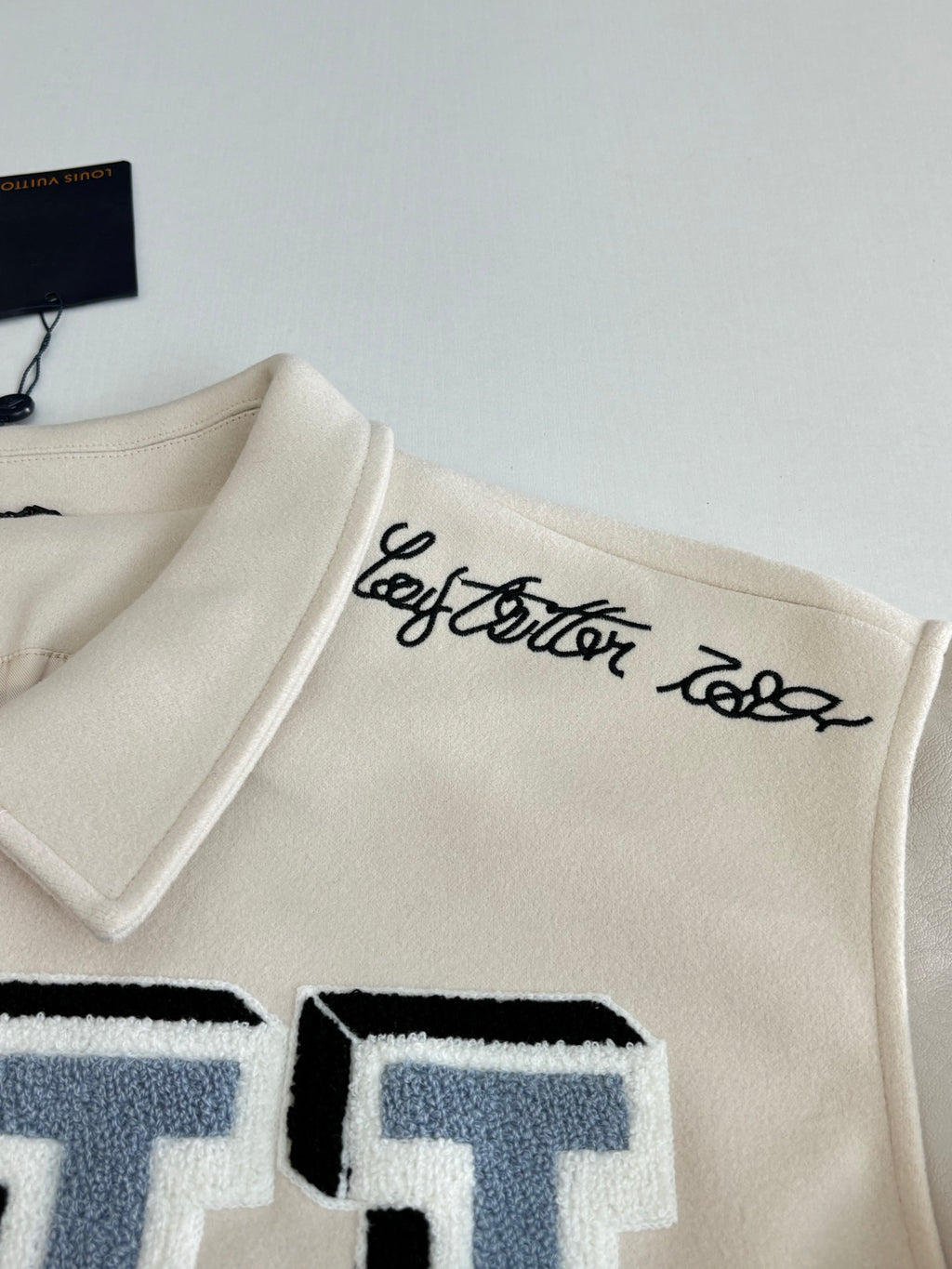 Louis Vuitton cream jacket collar with black script logo and blue letter patch