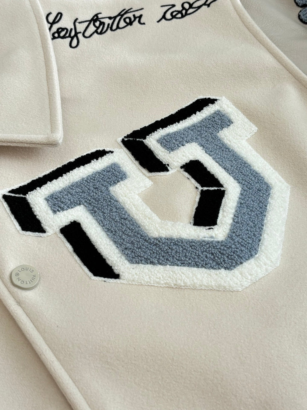 Louis Vuitton cream jacket close-up of large blue letter patch on chest