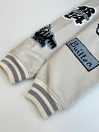 Cream long-sleeve jacket with patch graphics and striped ribbed cuffs