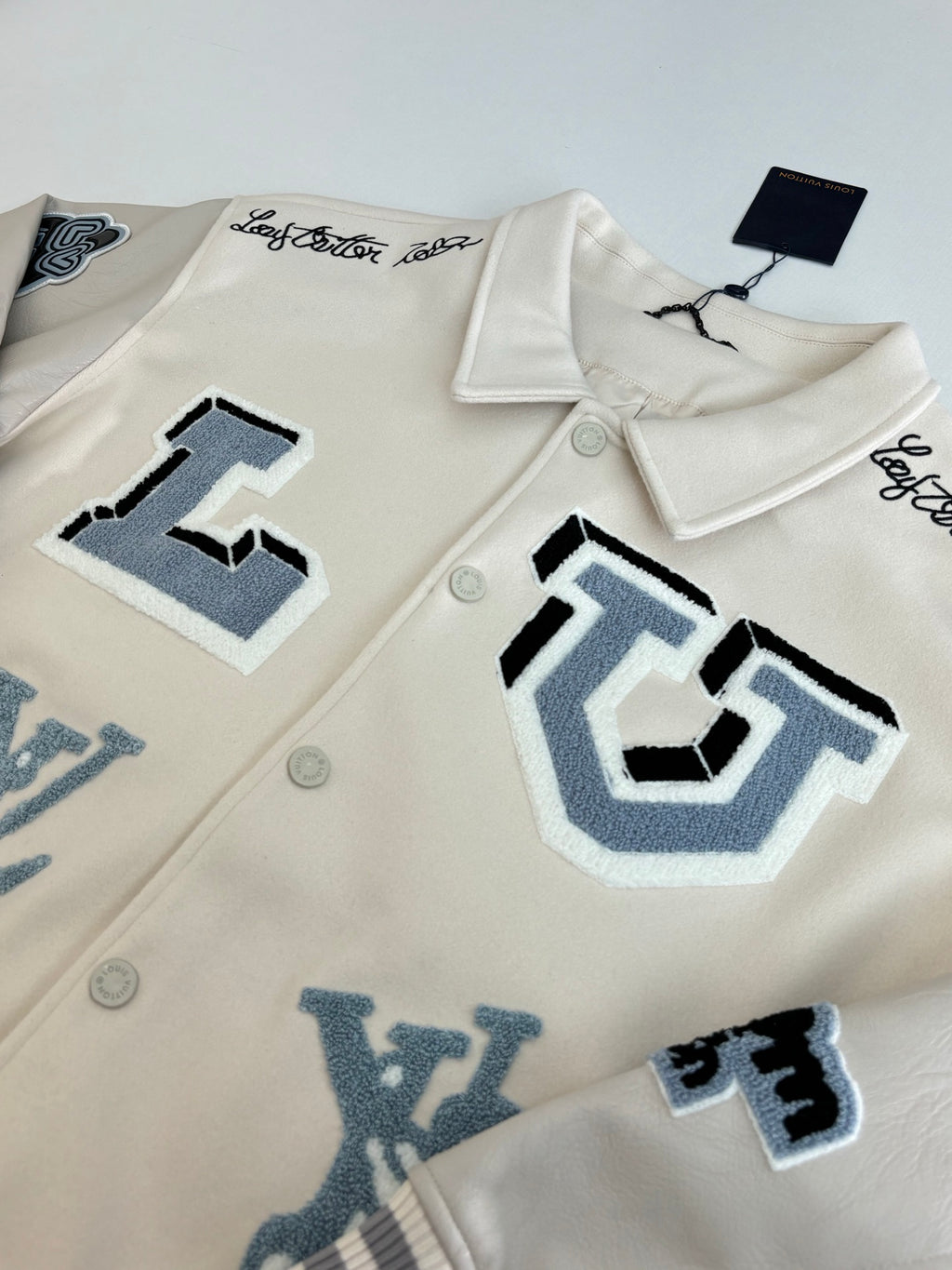 Louis Vuitton cream jacket close-up with blue applique graphics and snap buttons