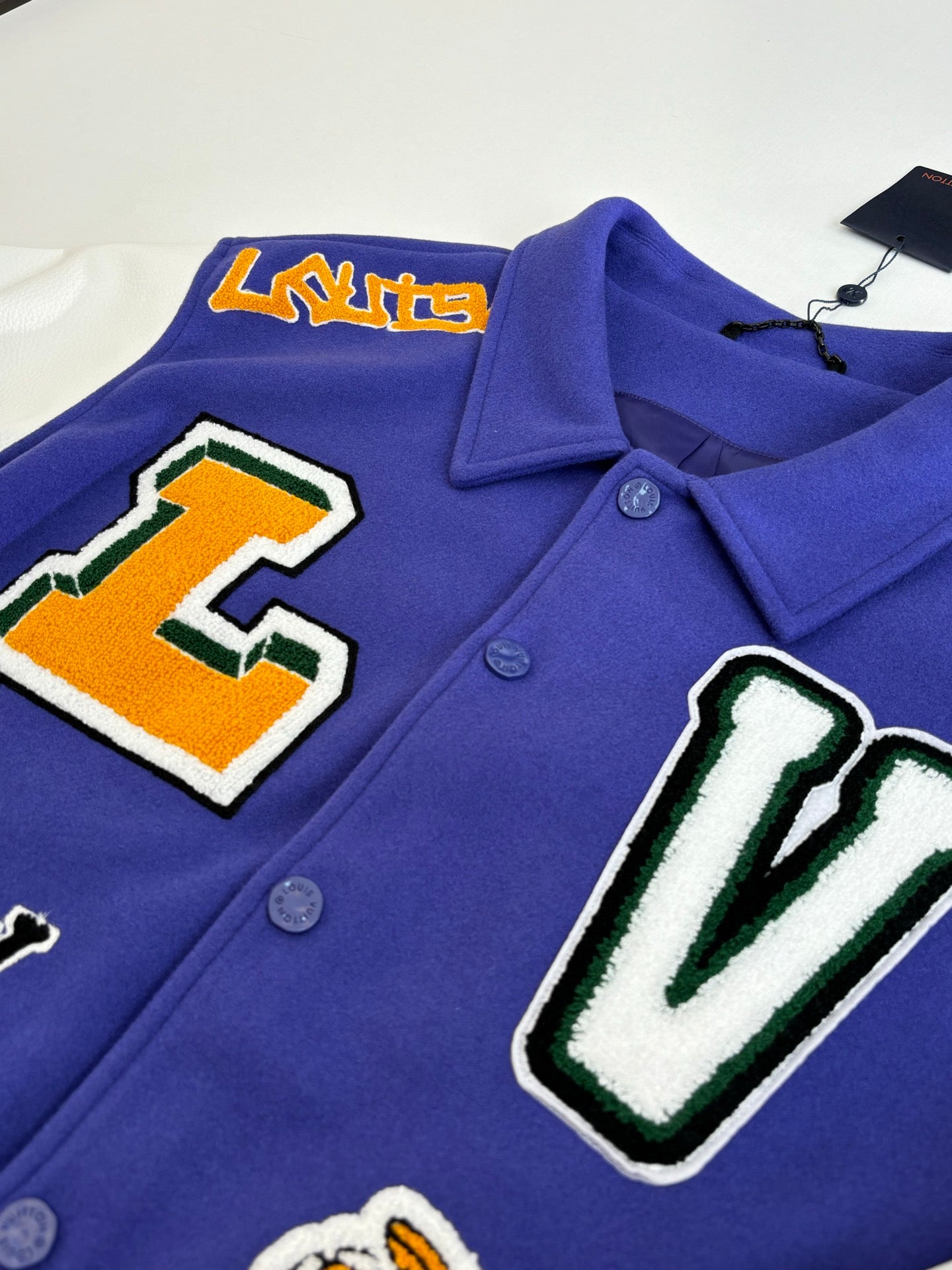 Blue varsity jacket close-up with embroidered L and V patches and snap buttons