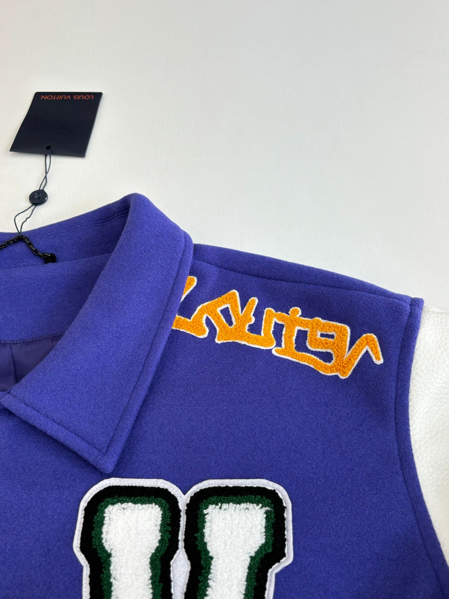 Blue jacket shoulder and sleeve panel with arched embroidered logo and green-outlined V