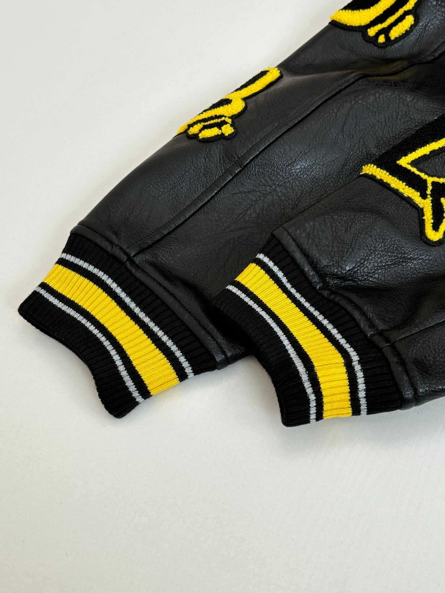Black long jacket cuff with yellow-and-white striped ribbing and applique detail