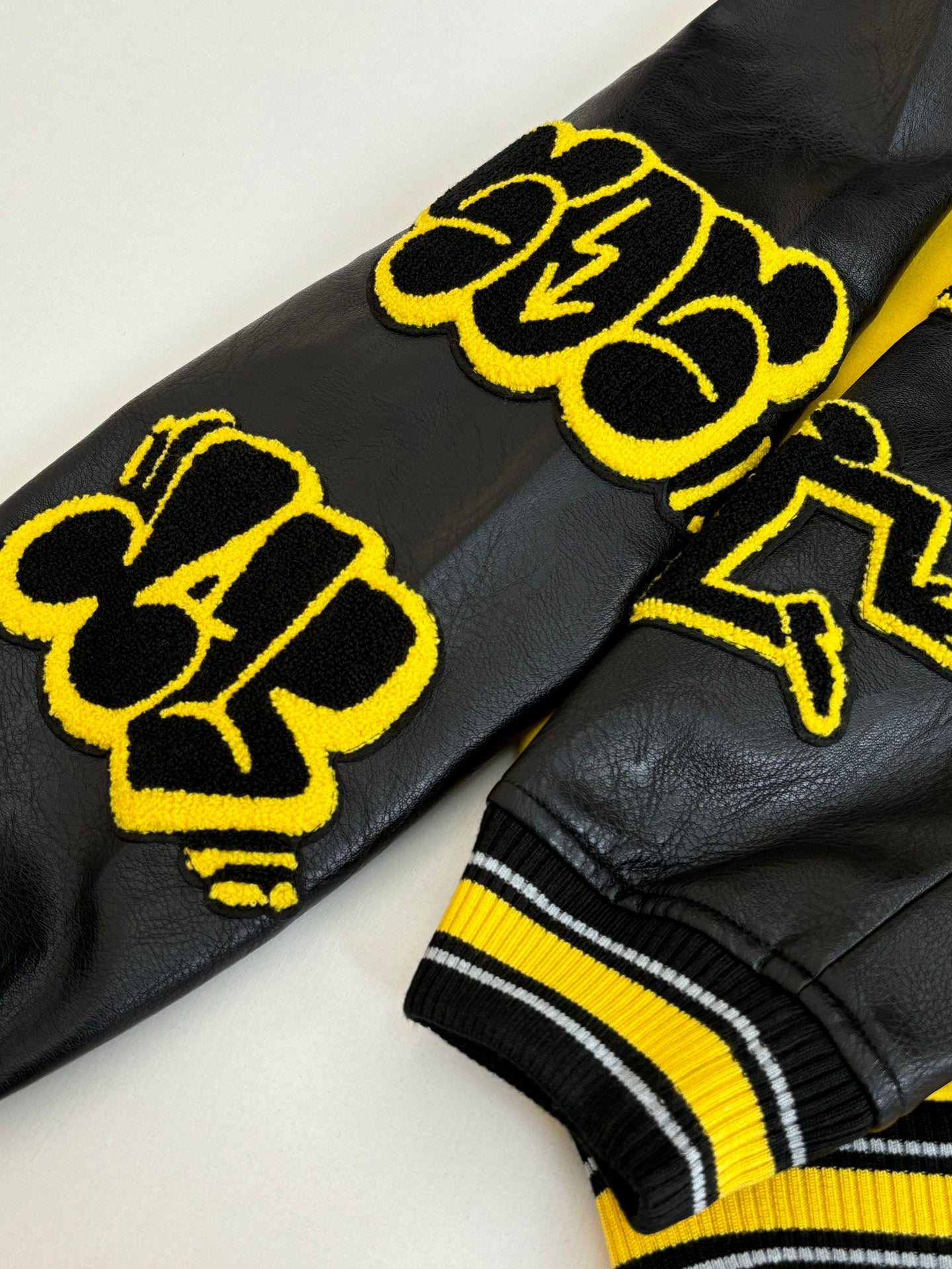 Black long jacket with yellow embroidered logo patches and ribbed striped cuffs