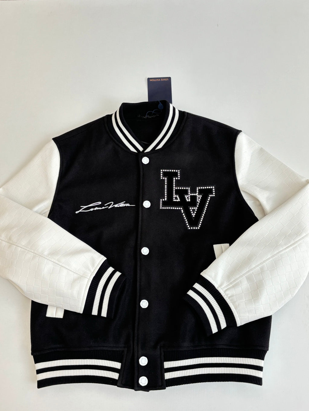 Louis Vuitton varsity jacket front, black with white sleeves, LV logo and snap buttons.
