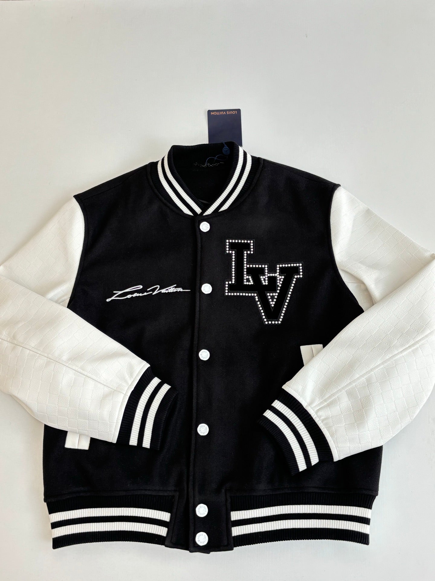 Louis Vuitton varsity jacket front, black with white sleeves, LV logo and snap buttons.