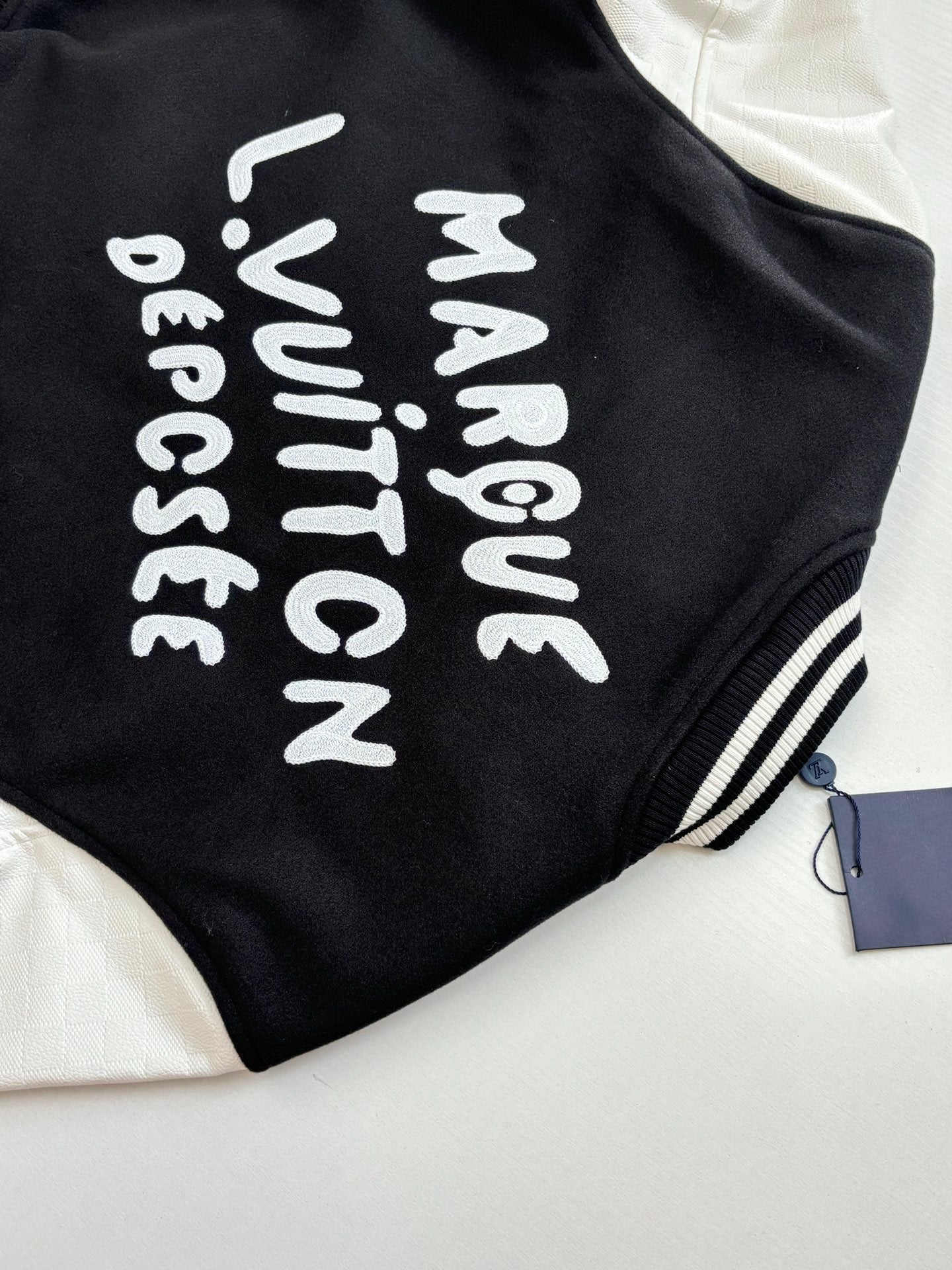 Louis Vuitton varsity jacket back, black with white vertical text graphic.