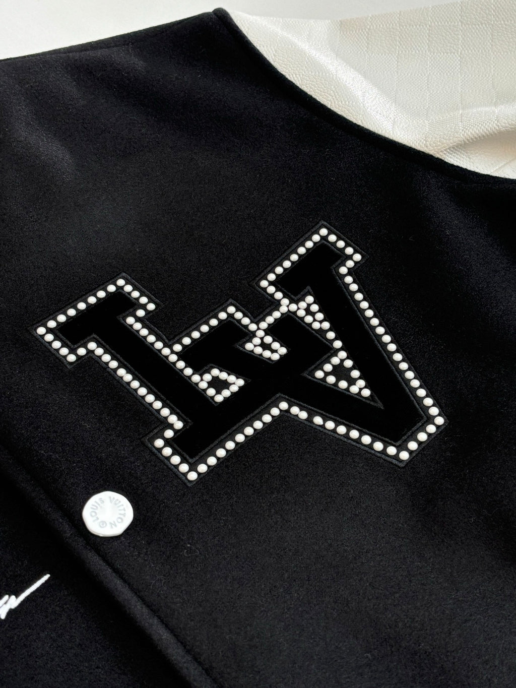 Louis Vuitton varsity jacket detail, black with rhinestone-style arched logo lettering.