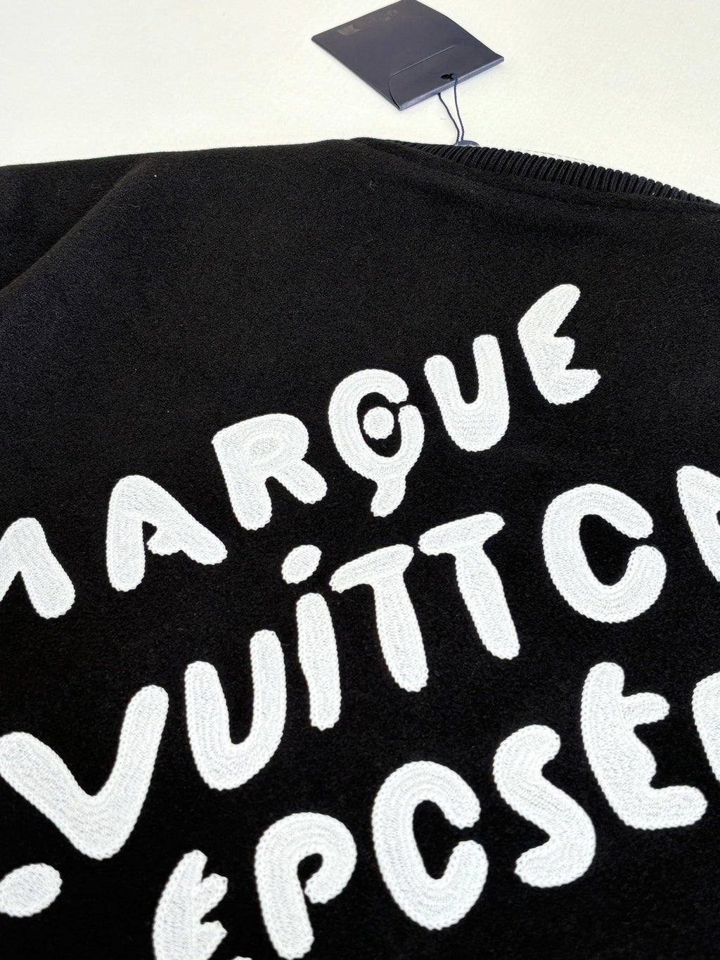 Louis Vuitton varsity jacket back graphic close-up, black with large white lettering.