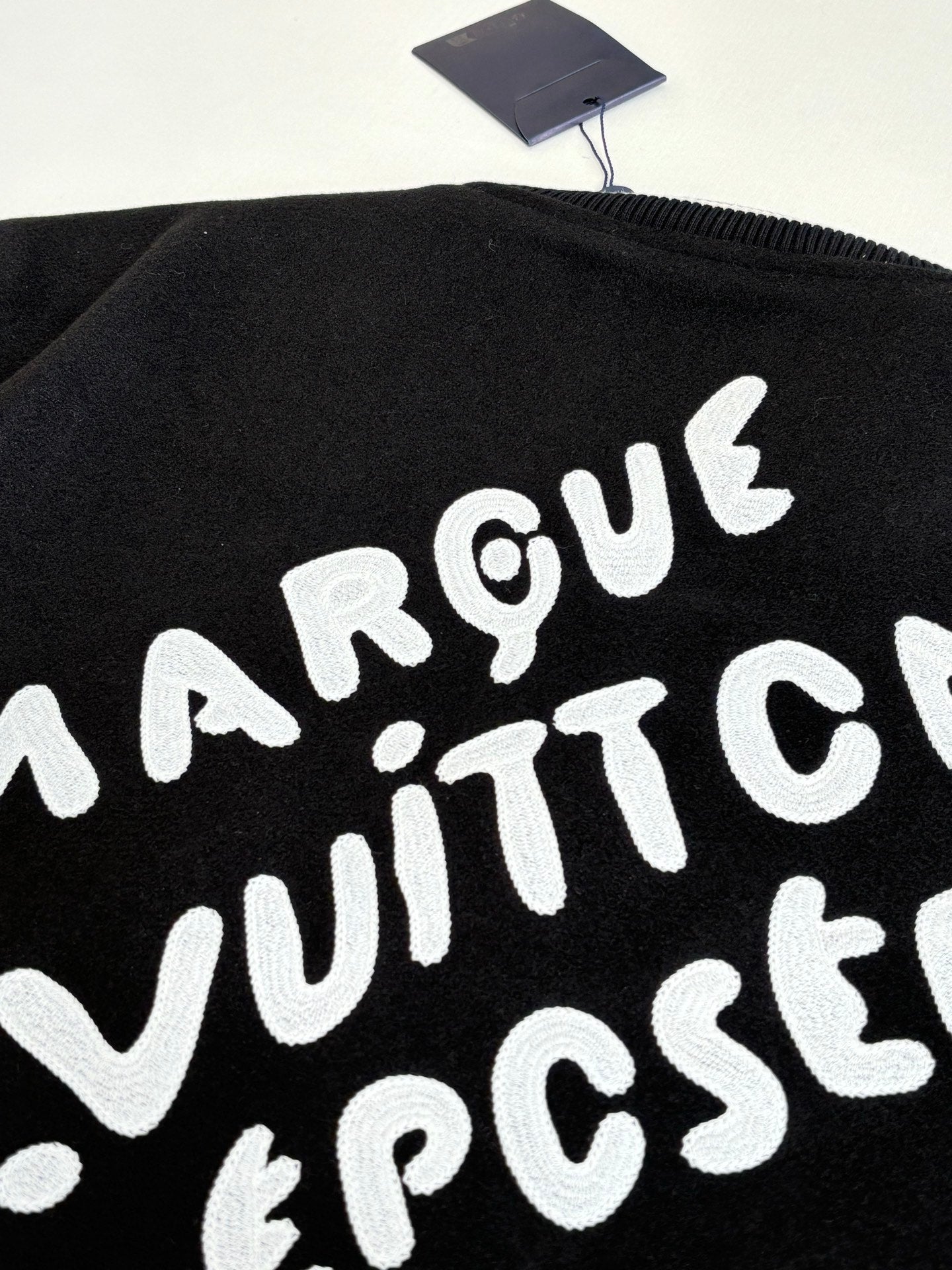 Louis Vuitton varsity jacket back graphic close-up, black with large white lettering.