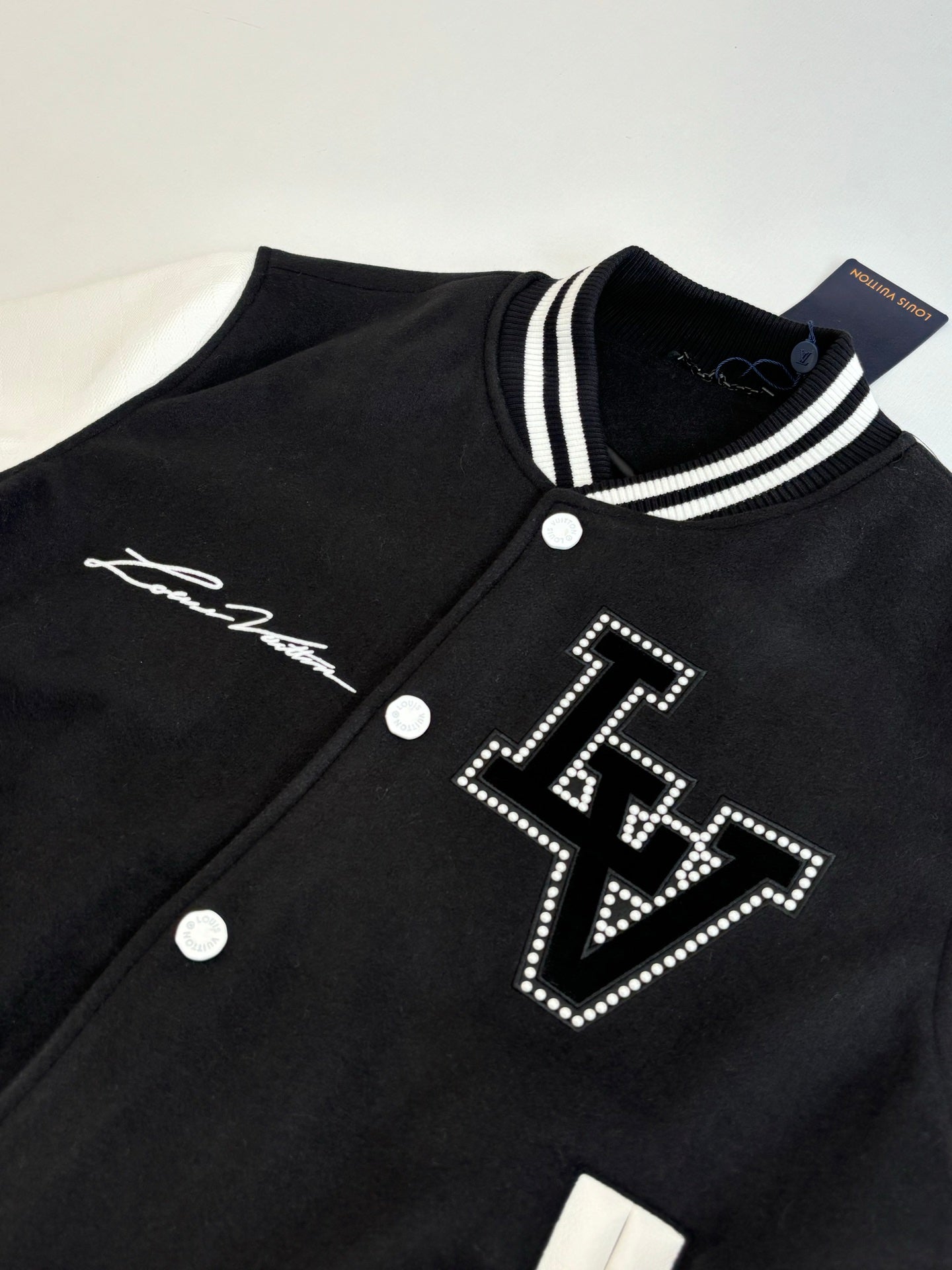 Louis Vuitton varsity jacket close-up, black with white striped collar and studded logo.