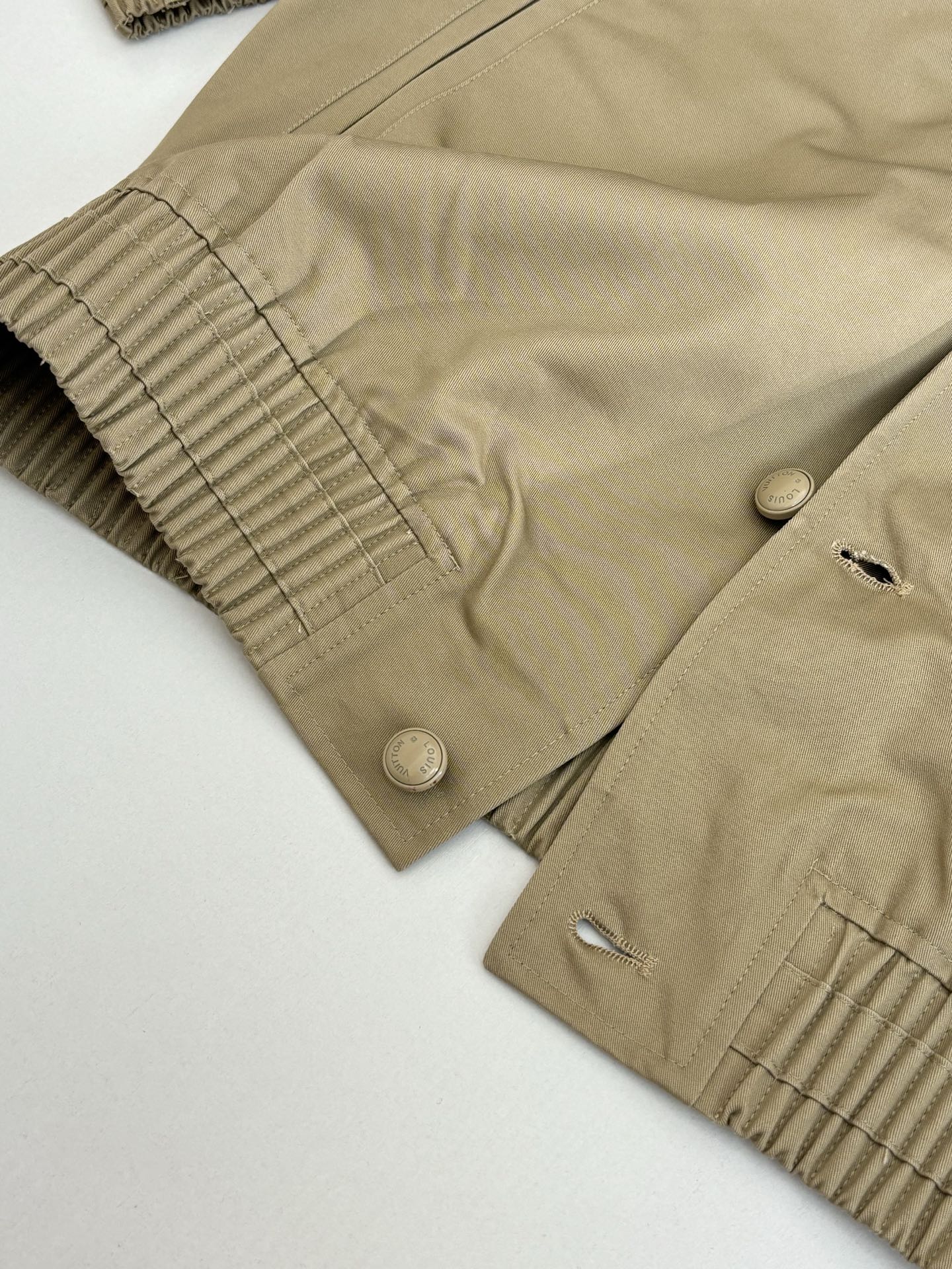Tan bomber jacket close-up of ribbed cuff, snap buttons, and curved seams