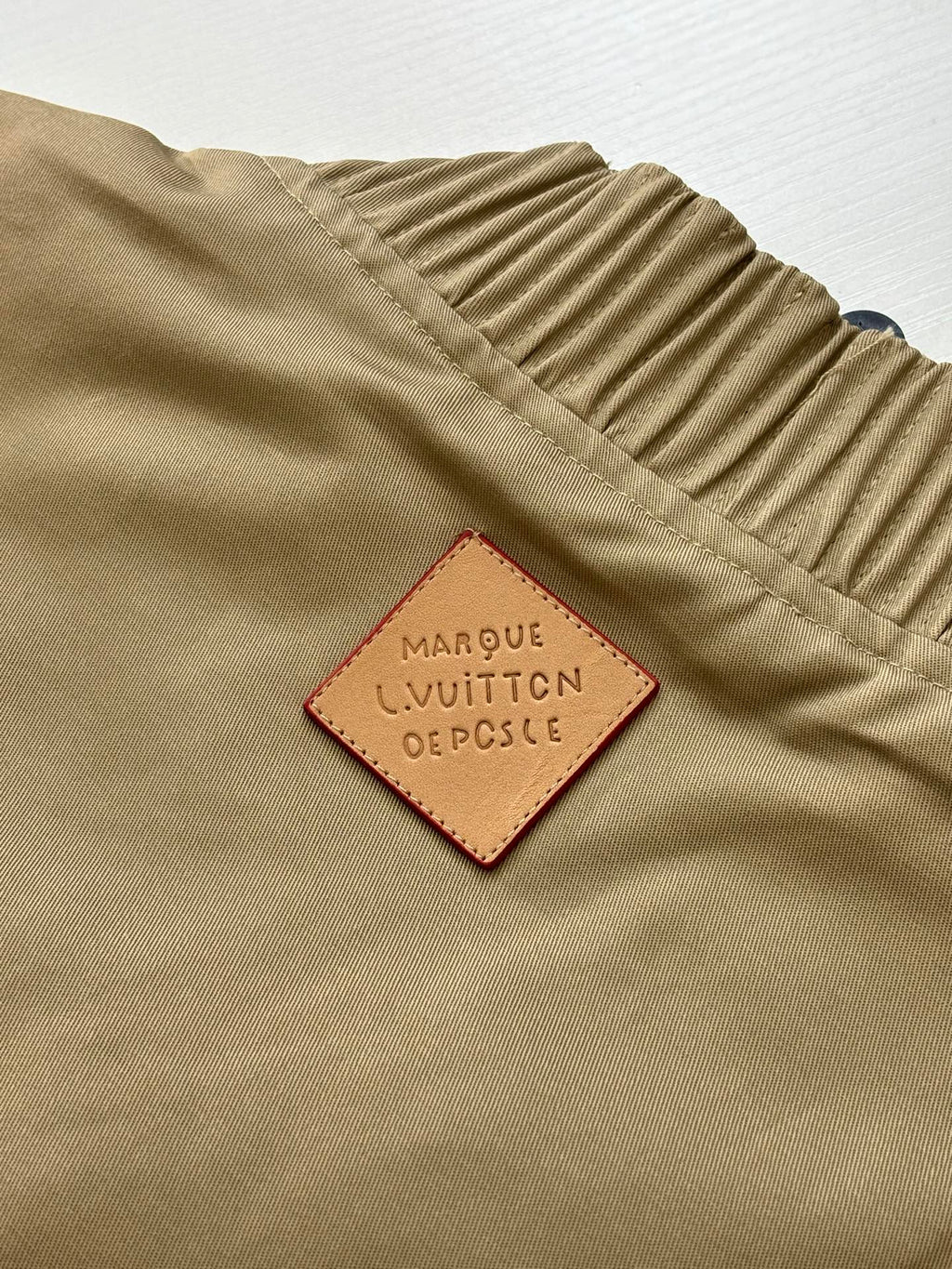 Tan bomber jacket label patch reading Louis Vuitton and dot symbol details