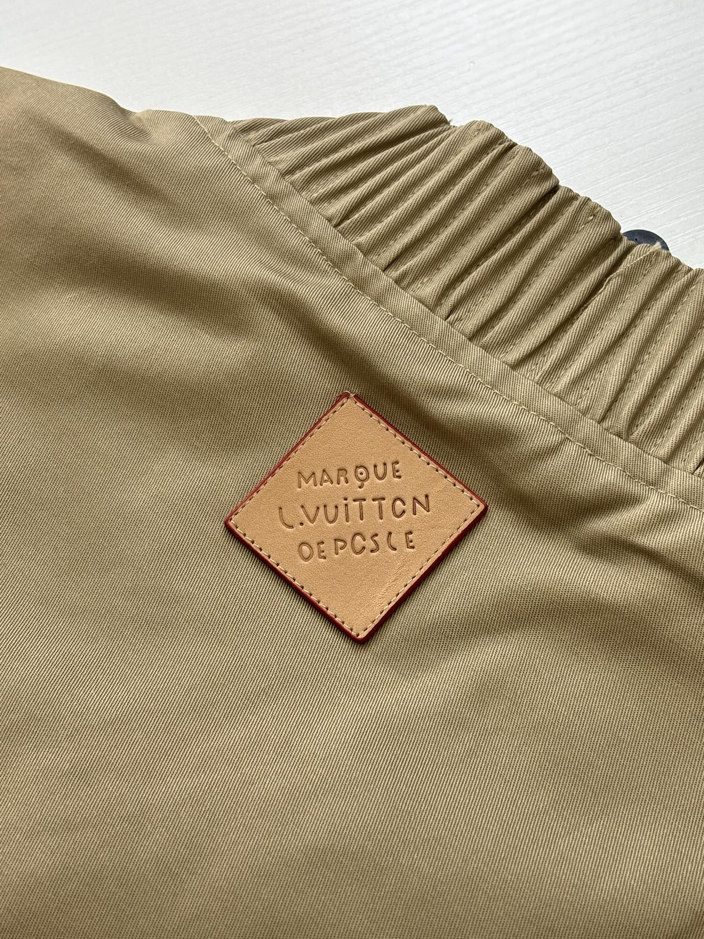 Tan bomber jacket label patch reading Louis Vuitton and dot symbol details