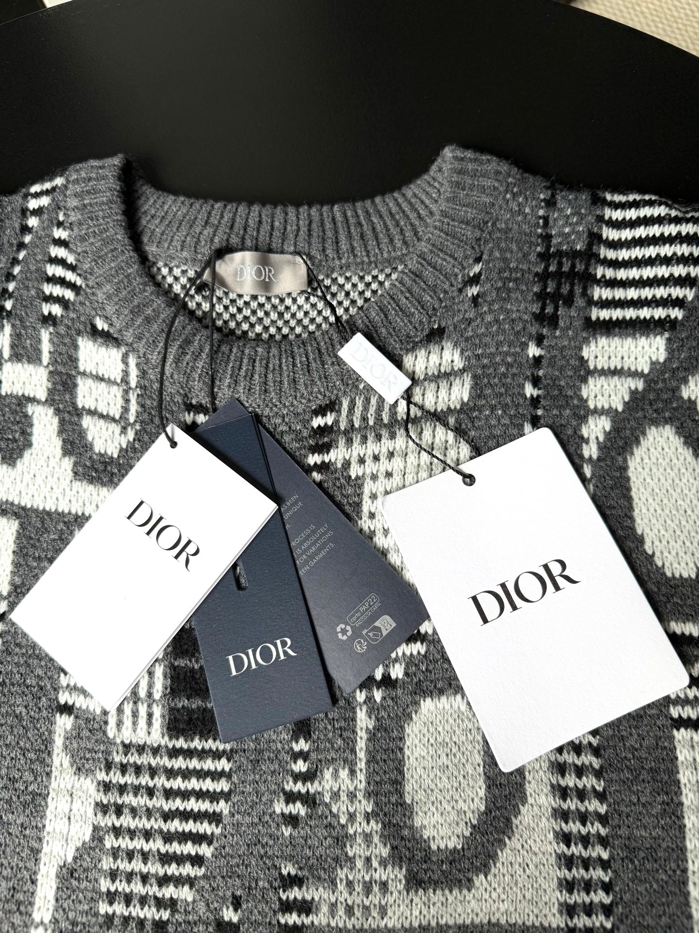 Gray knit sweater with black-and-white logo pattern and Dior hang tags