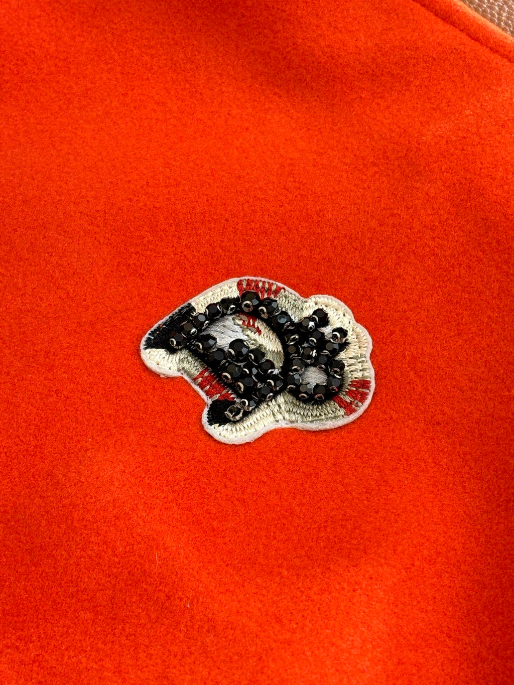 Orange fabric varsity jacket with embroidered crest patch on chest