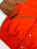 Orange varsity jacket detail with ribbed cuff, brown striped trim, snap buttons