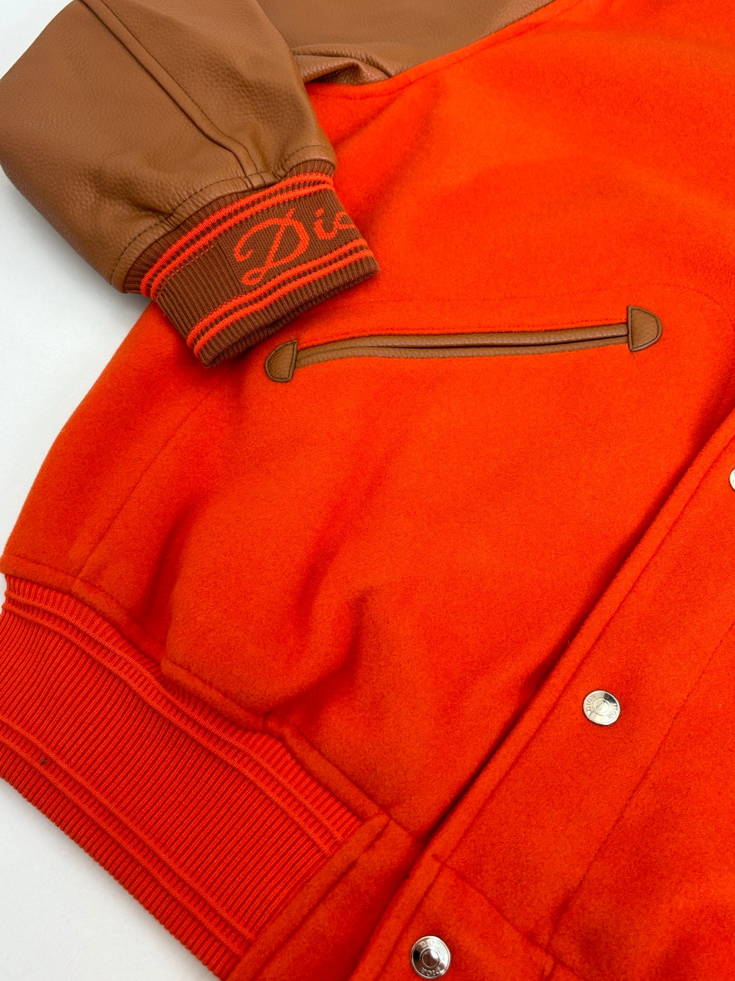 Orange varsity jacket detail with ribbed cuff, brown striped trim, snap buttons