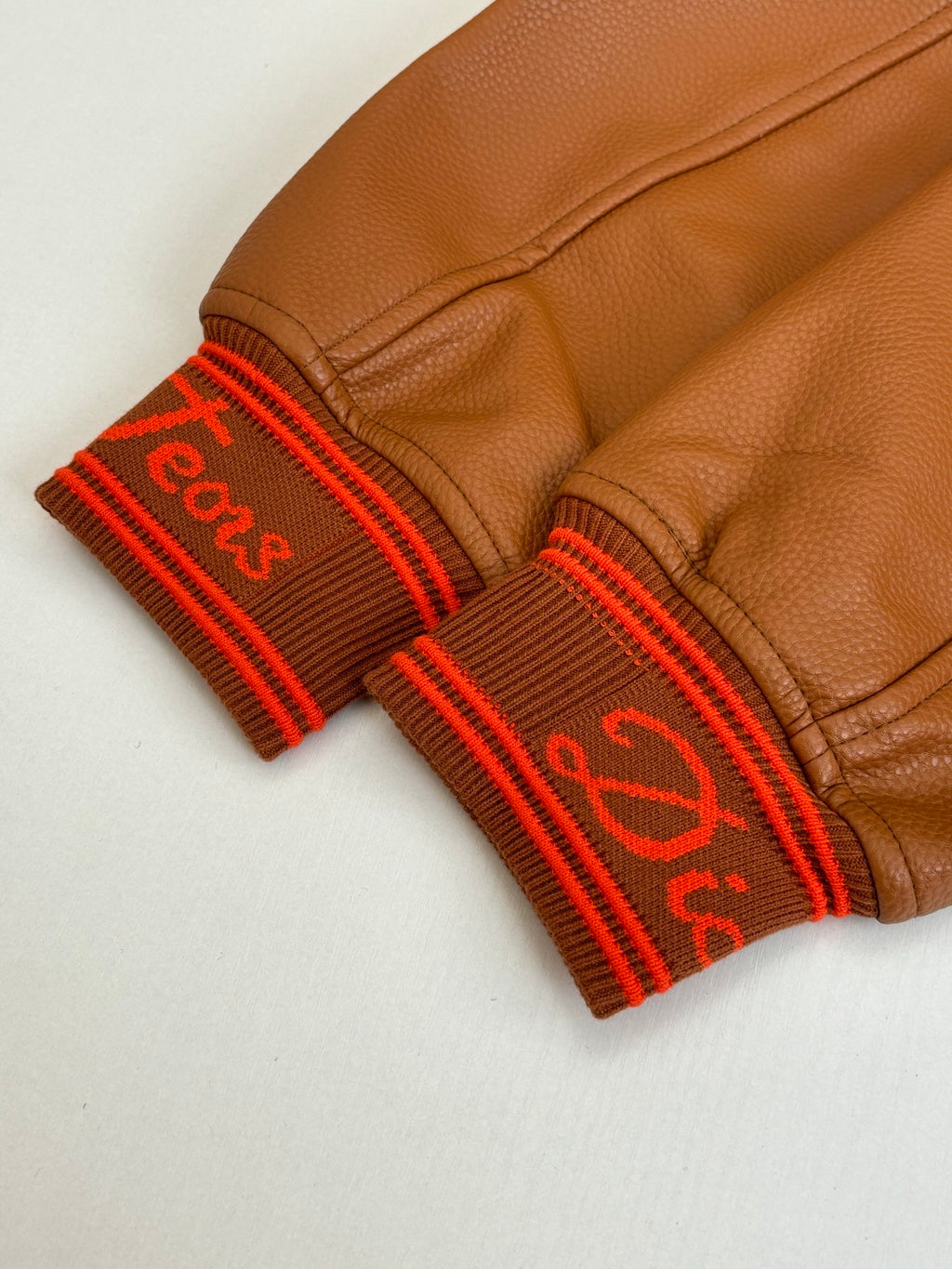 Brown leather cuffs with red ribbed trim and stitched logo lettering