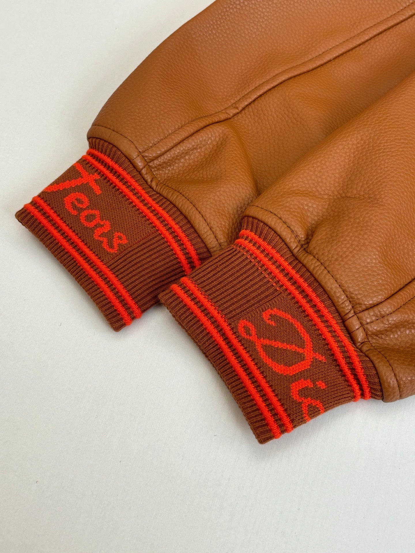 Brown leather cuffs with red ribbed trim and stitched logo lettering