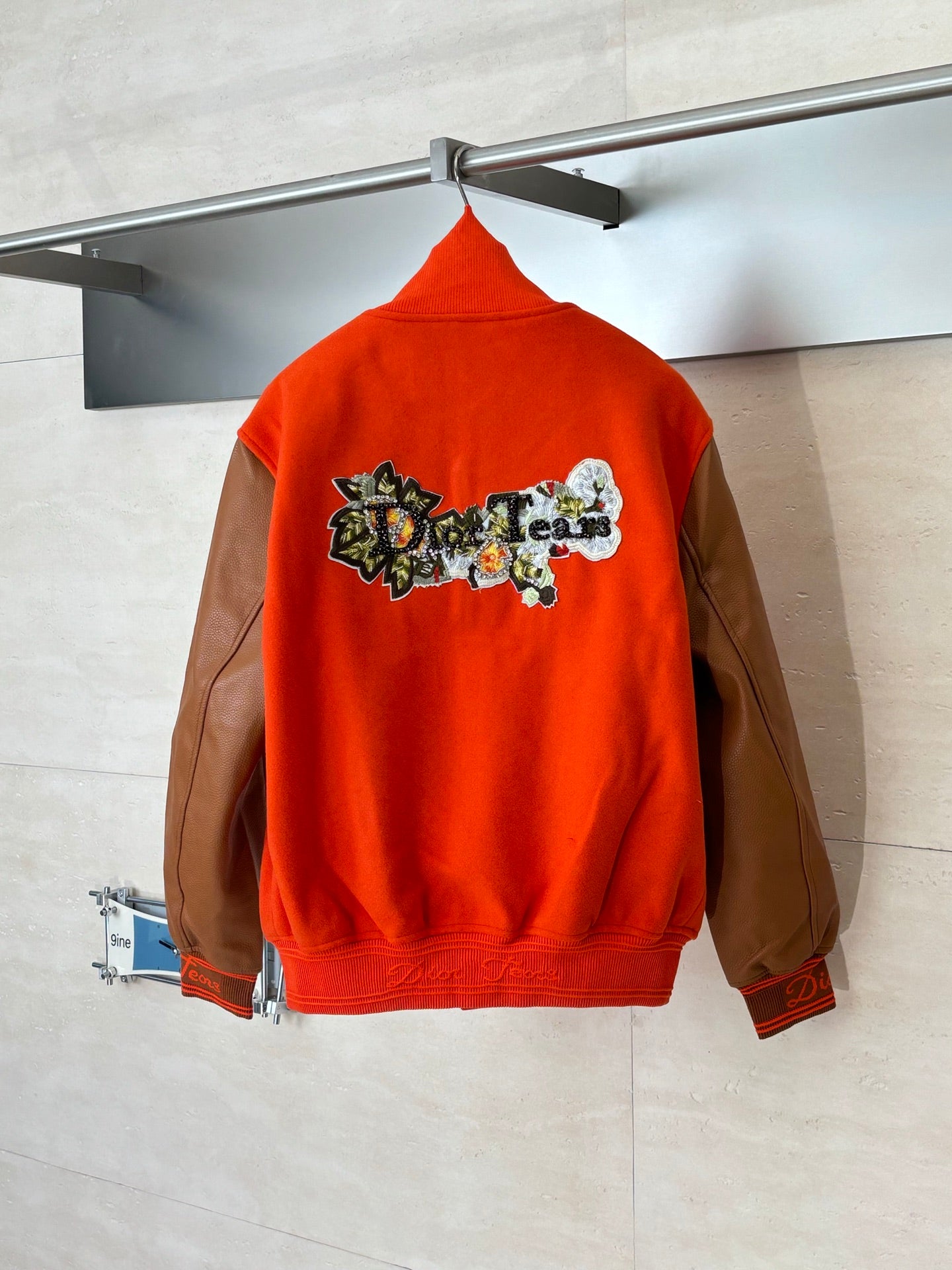 Orange varsity jacket with brown sleeves, embroidered back graphic, snap front