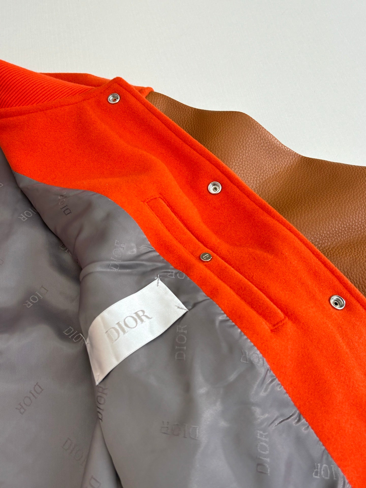 Orange varsity jacket interior lining view with Dior-branded fabric and snaps