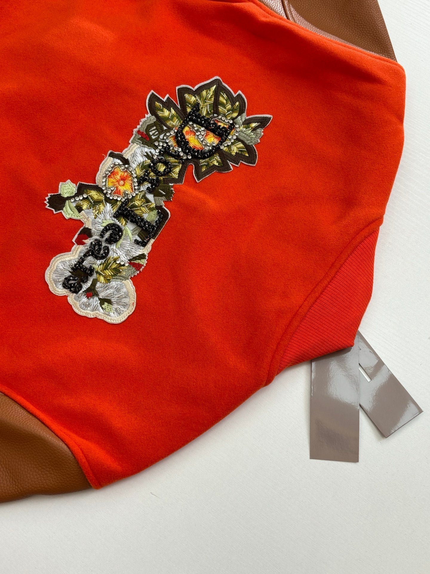 Orange jacket with large ornate embroidered chest patch and brown leather sleeve panel