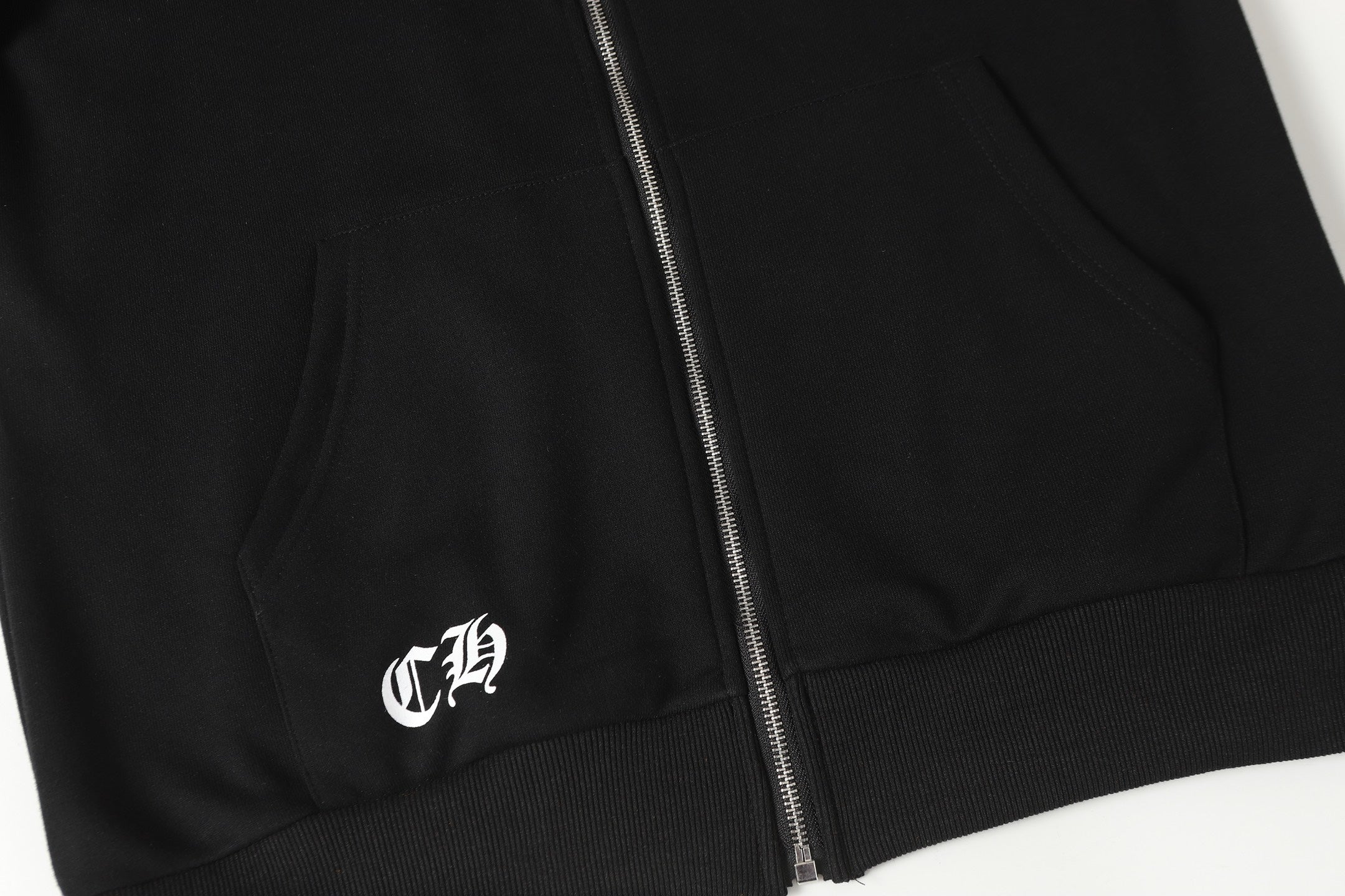 Black hoodie lower front zipper and hem with small white logo mark.