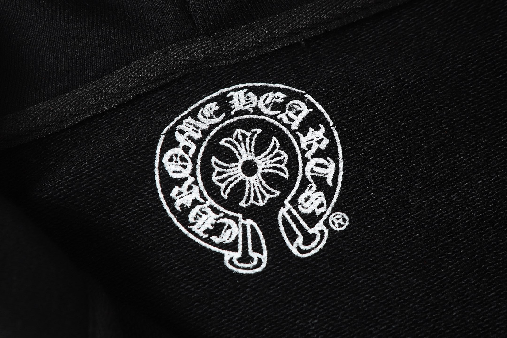 Black hoodie fabric with white circular crest logo print.