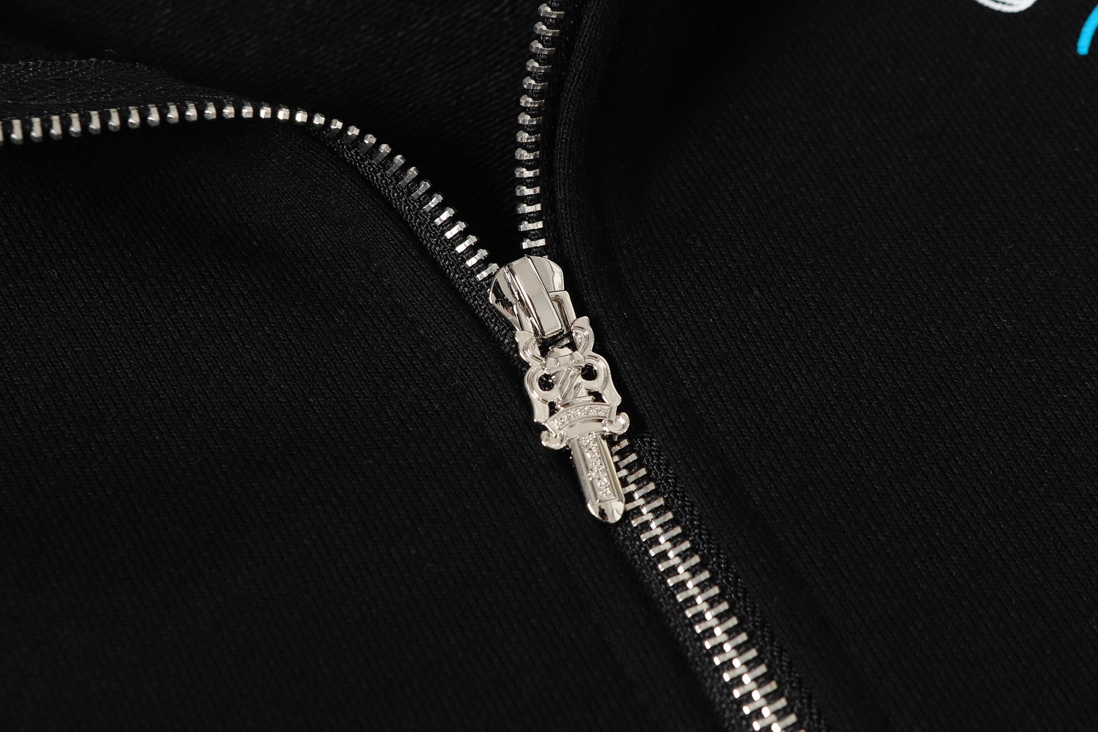 Black hoodie close-up of front zipper with shiny metal pull and teeth.