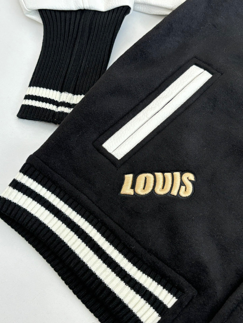 Louis Vuitton varsity jacket sleeve cuff close-up with ribbed stripes and gold “LOUIS” lettering